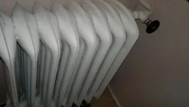 Starý bílý radiátor s odvzdušňovacím ventilem na stěně.