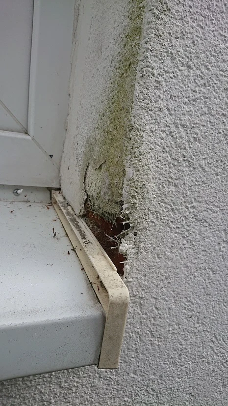 Poškozená fasáda s odlupujícím se omítkou u okna.