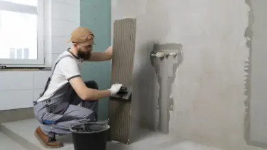 Muž nanáší tmel na desku v koupelně během hydroizolace.