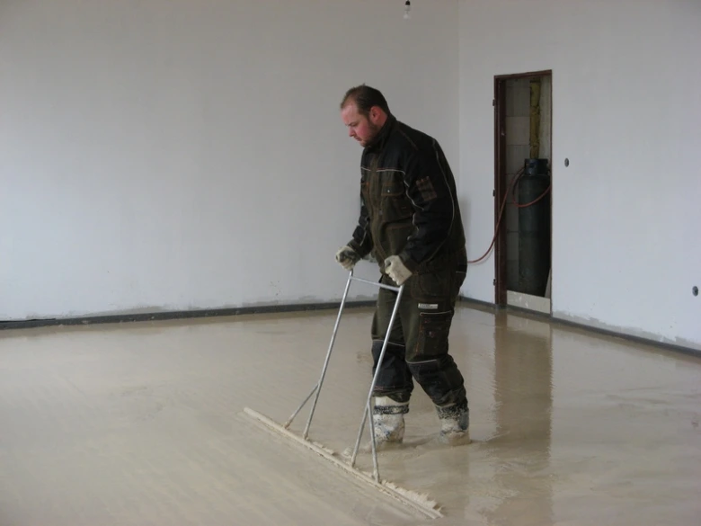Pracovník roztírá samonivelační podlahu v místnosti.