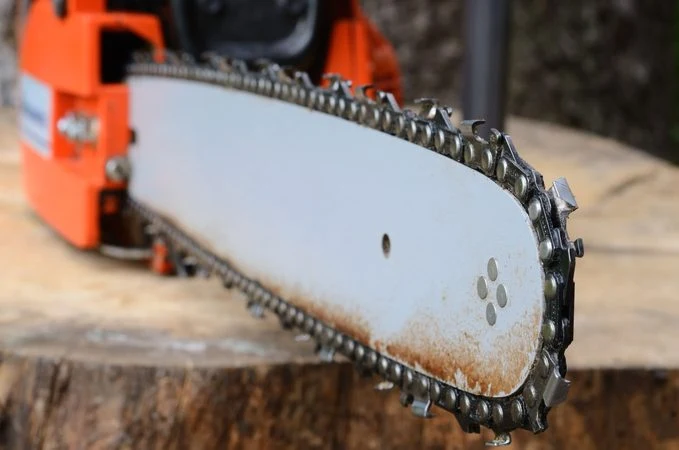 Detail motorové pily ukazující směr zubů řetězu na liště.