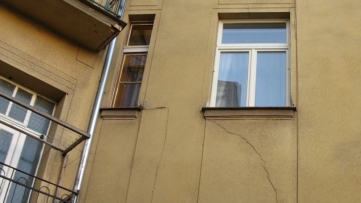 Trhliny ve zdivu fasády bytového domu s okny.