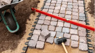 Kladení dlažebních kostek na písek s nástroji pro stavbu chodníku.