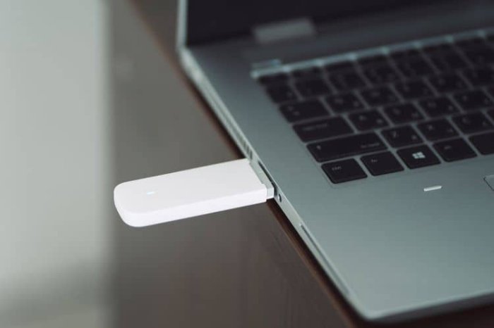Bílý USB adaptér pro Wi-Fi zapojený do bočního portu notebooku.