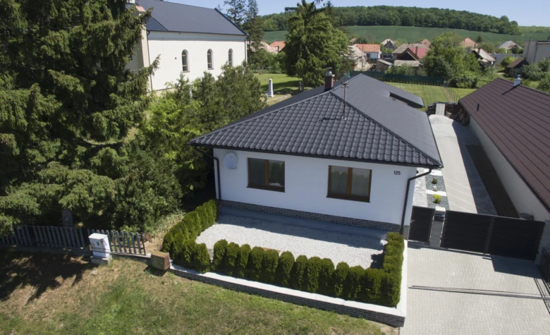 Moderní dům s tmavou taškovou střechou v českém venkovském prostředí.