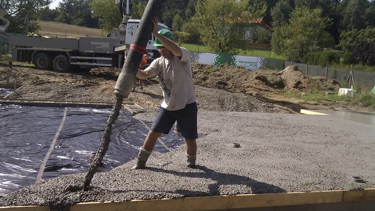 Stavebník nalévá beton do základové formy na staveništi.