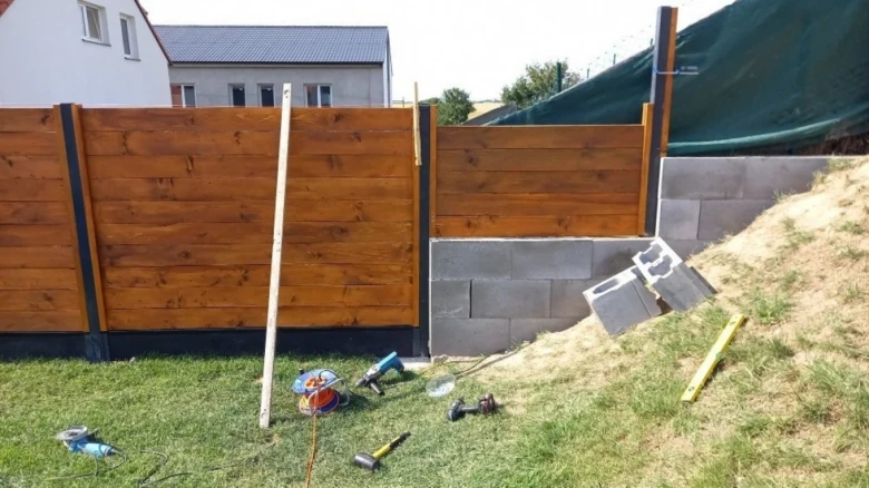 Stavba dřevěného plotu na svahu s nástroji a cihlami