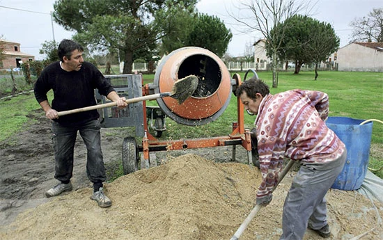 Dva muži míchají maltu pro zdivo pomocí betonu smíchavače.