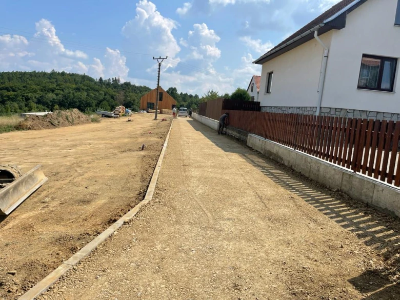 Stavba příjezdové cesty vedle domu s dřevěným plotem.