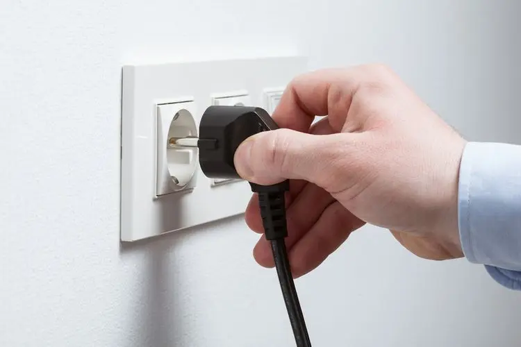 Ruka zapojuje elektrickou zástrčku do zásuvky na zdi.