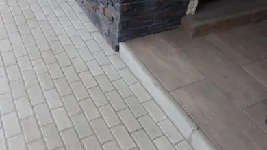 Světlá dlažba chodníku vedle domu s kamenným obkladem.
