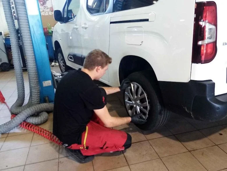 Mechanik utahuje šrouby na kolesu bílého auta.