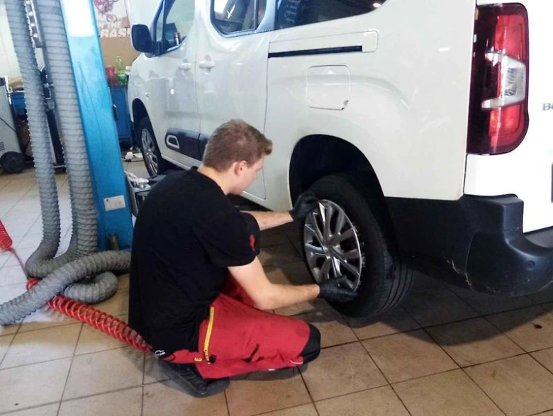 Mechanik povoluje šrouby na kolo bílého vozu.