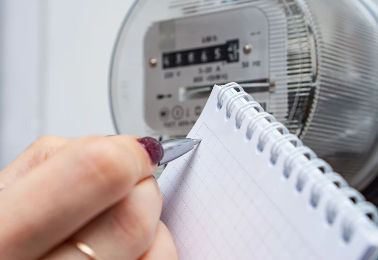 Ruka zapisuje čísla z elektroměru do sešitu pro výpočet spotřeby.