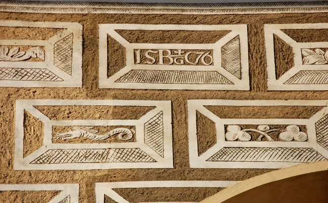 Detail psaníčkového sgrafita na zdi s bílými reliéfními motivy.