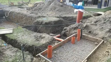 Výkop pro bazénovou filtraci s oranžovými hadicemi v štěrku.