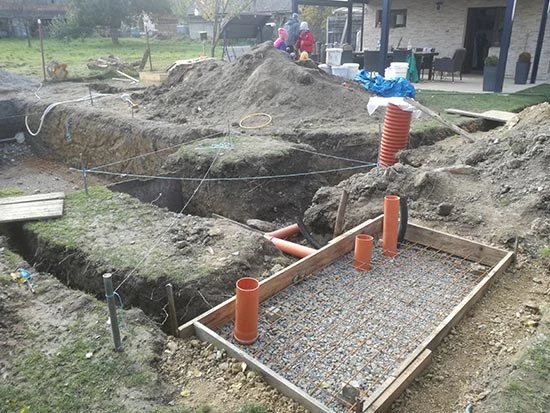 Výkop pro bazénovou filtraci s oranžovými hadicemi v štěrku.