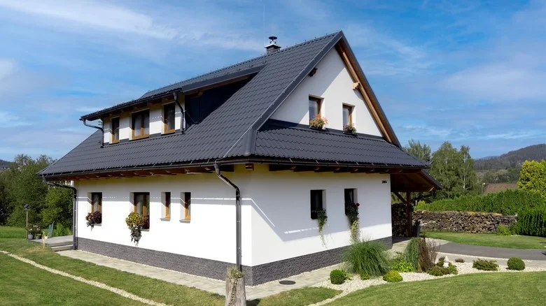 Dokončená montáž plechové střechy na bílém domě s doplňky.