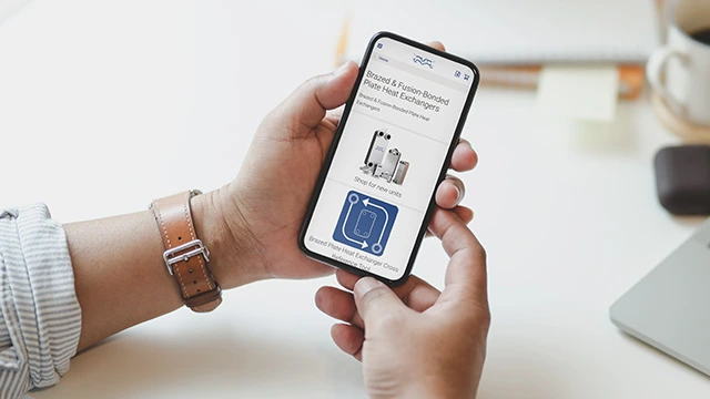 Ruce drží chytrý telefon s aplikací o výměnících tepla voda-voda.