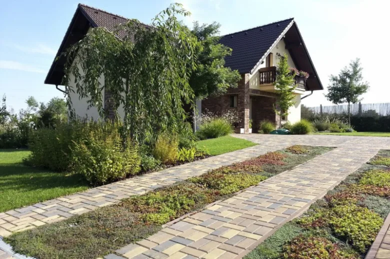 Příjezdová cesta k domu s kamenným dlažbou a zelení.