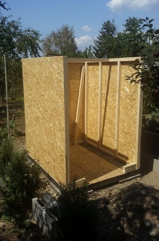 Zahradní domek z osb desek v procesu stavby na zahradě.