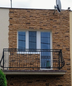 Fotografie fasády domu s cihlovou zdí a balkónem.