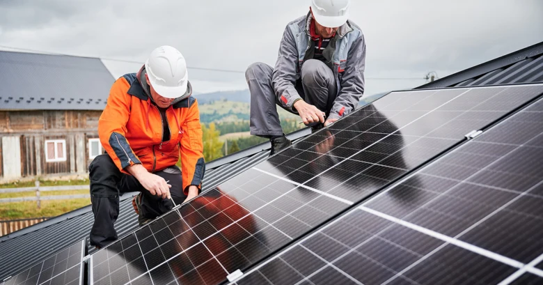 Dva pracovníci montují fotovoltaické panely na střechu pod optimálním úhlem.