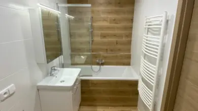 Bílá koupelna s dřevěnými prvky na podlaze i v obkladu.