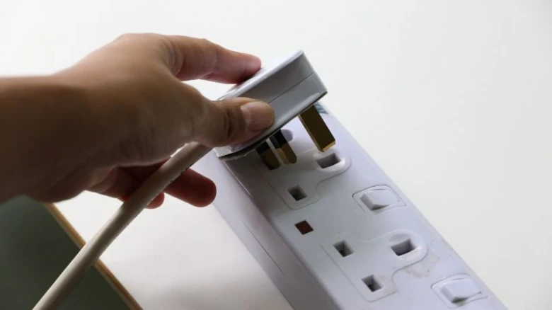 Ruka zapojuje britskou zásuvku do elektrického rozvodného panelu.