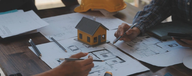 Architekti pracují s plány domu při schůzce o projektu.