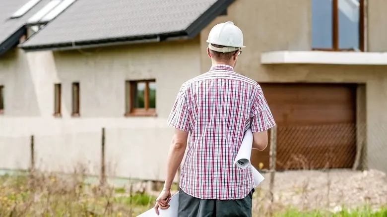 Architekt s plány stojí před domem v procesu revitalizace.