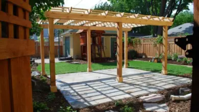 Nová dřevěná pergola s betonovou dlažbou v zahradním pozadí.