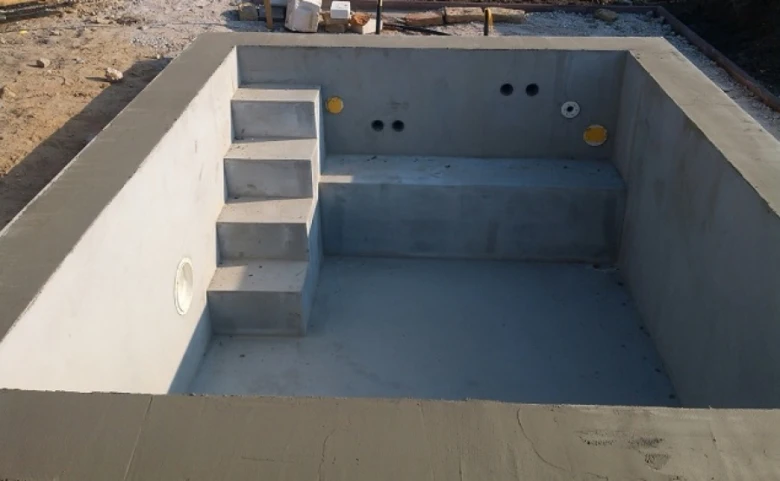 Nově postavený betonový bazén s vnitřními schody a otvory pro instalaci.