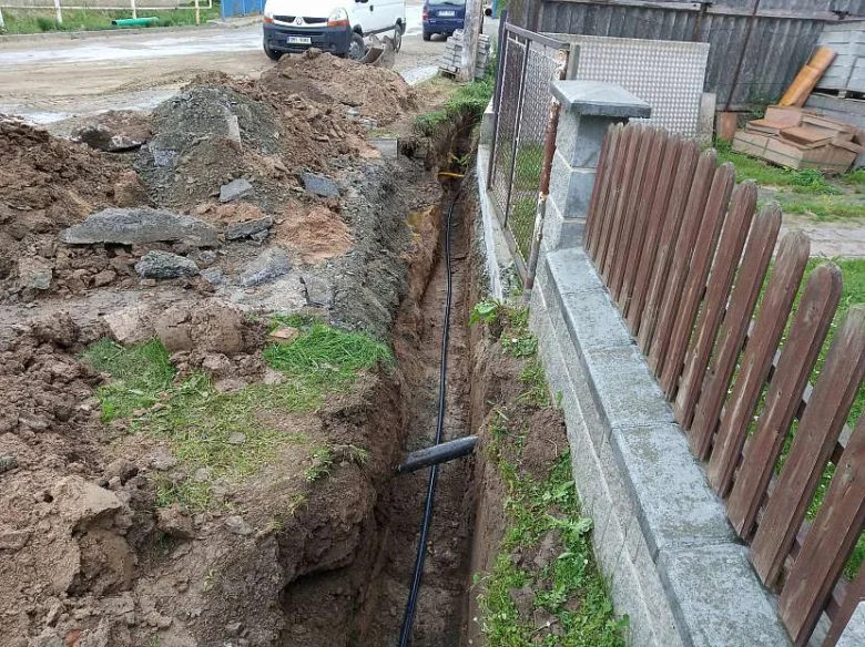 Zasazení vodovodního potrubí do vykopaného příkopu vedle plotu.