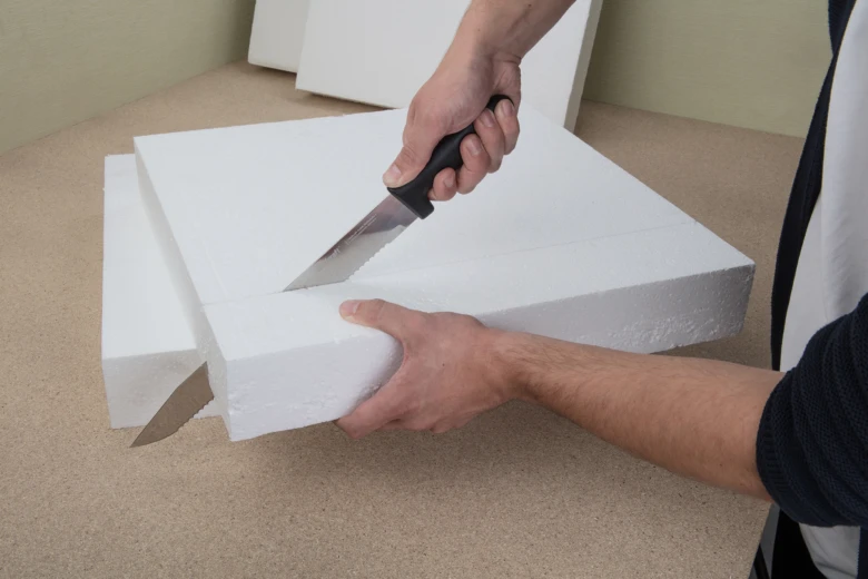 Muž řezá bílý styrofoam nožem na pracovní ploše.