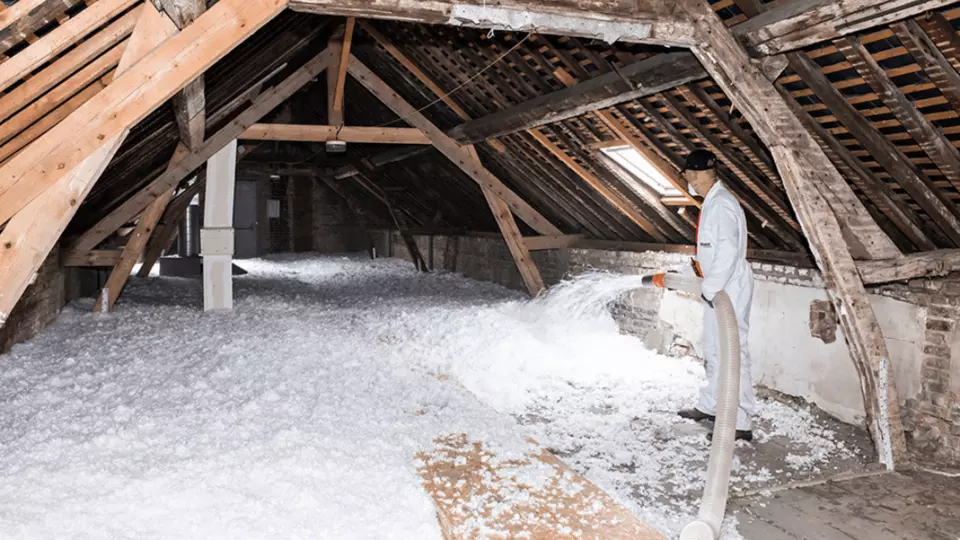 Pracovník fouká izolační materiál do střešního prostoru pomocí hadice.