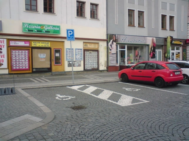 Červené auto na parkovacím místě s označeným přístupem pro invalidy.