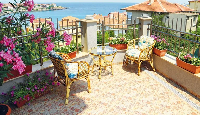 Přestavěný balkon s židlími, stolem a květinami při výhledu na moře.