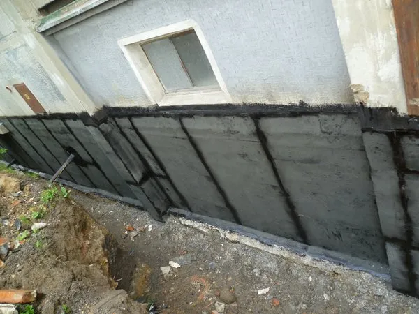 Instalace tepelné izolace do základů domu pomocí černých desek.