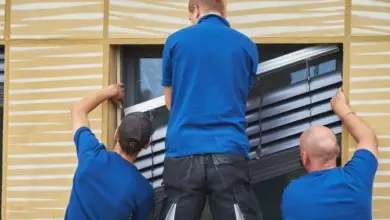 Tři muži montují venkovní žaluzie do okenního rámu.