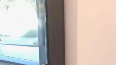 Detail tmavého rámu okna uvnitř místnosti s bílou stěnou.