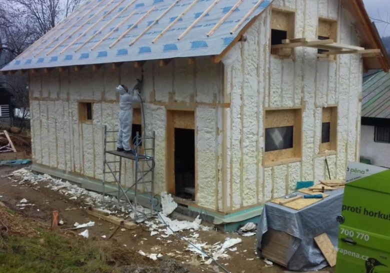 Stříkací pěna na dřevěný rám domu během stavby fasády.