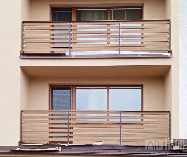Balkon s plotem z vodorovných dřevěných prken na fasádě budovy.