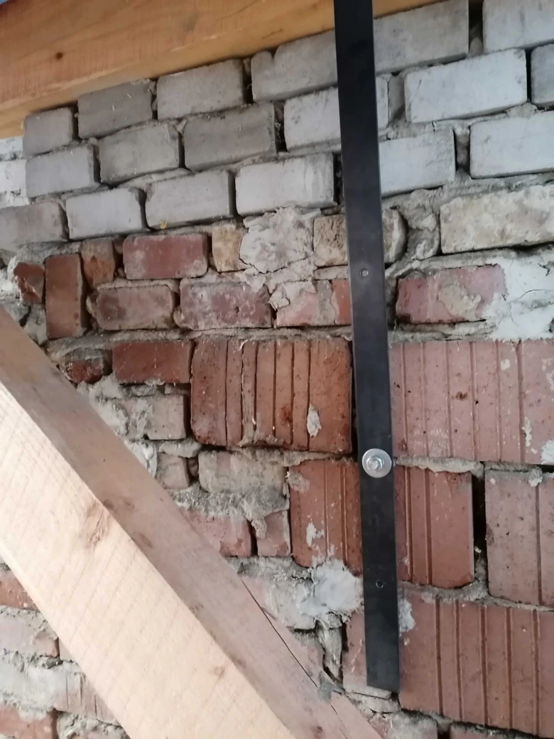 Černá kovová lišta kotvená k cihlové zdi šrouby.