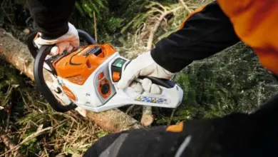 Osoba s motorovou pilou řezí větev v lese.