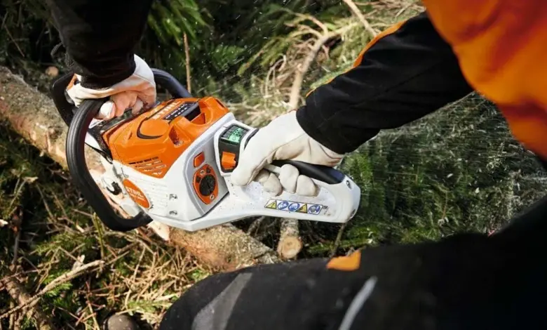 Osoba s motorovou pilou řezí větev v lese.