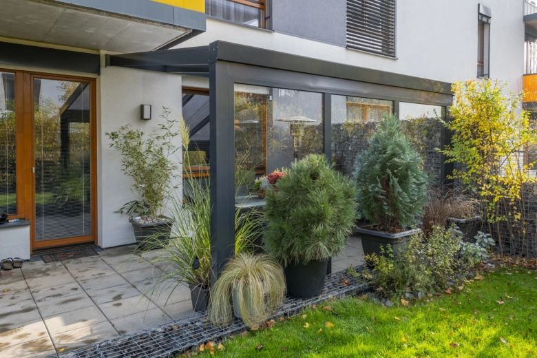 Moderní skleněná pergola s rostlinami na zahradě.