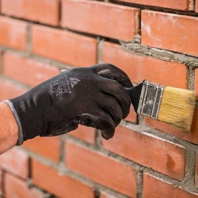 Ruka nanáší maltu na spoje v režném zdivu.