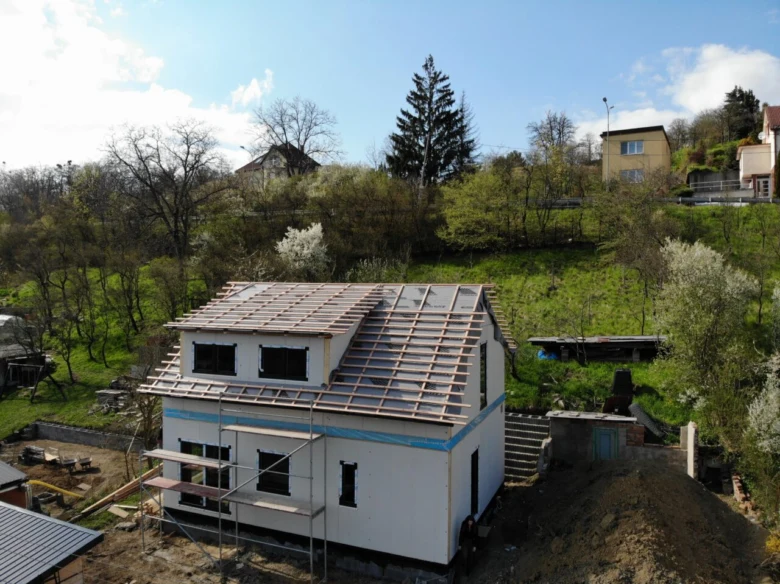 Dům v stavbě na kopci s viditelnou konstrukcí střechy.