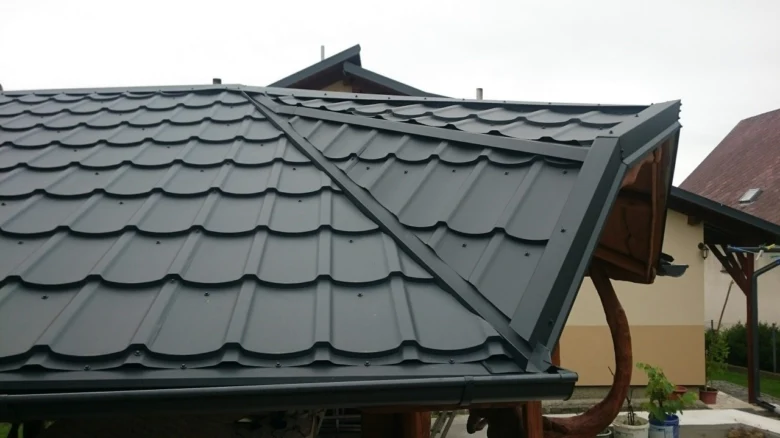 Detail tmavě šedých plechových střešní tašek na sklonu střechy.